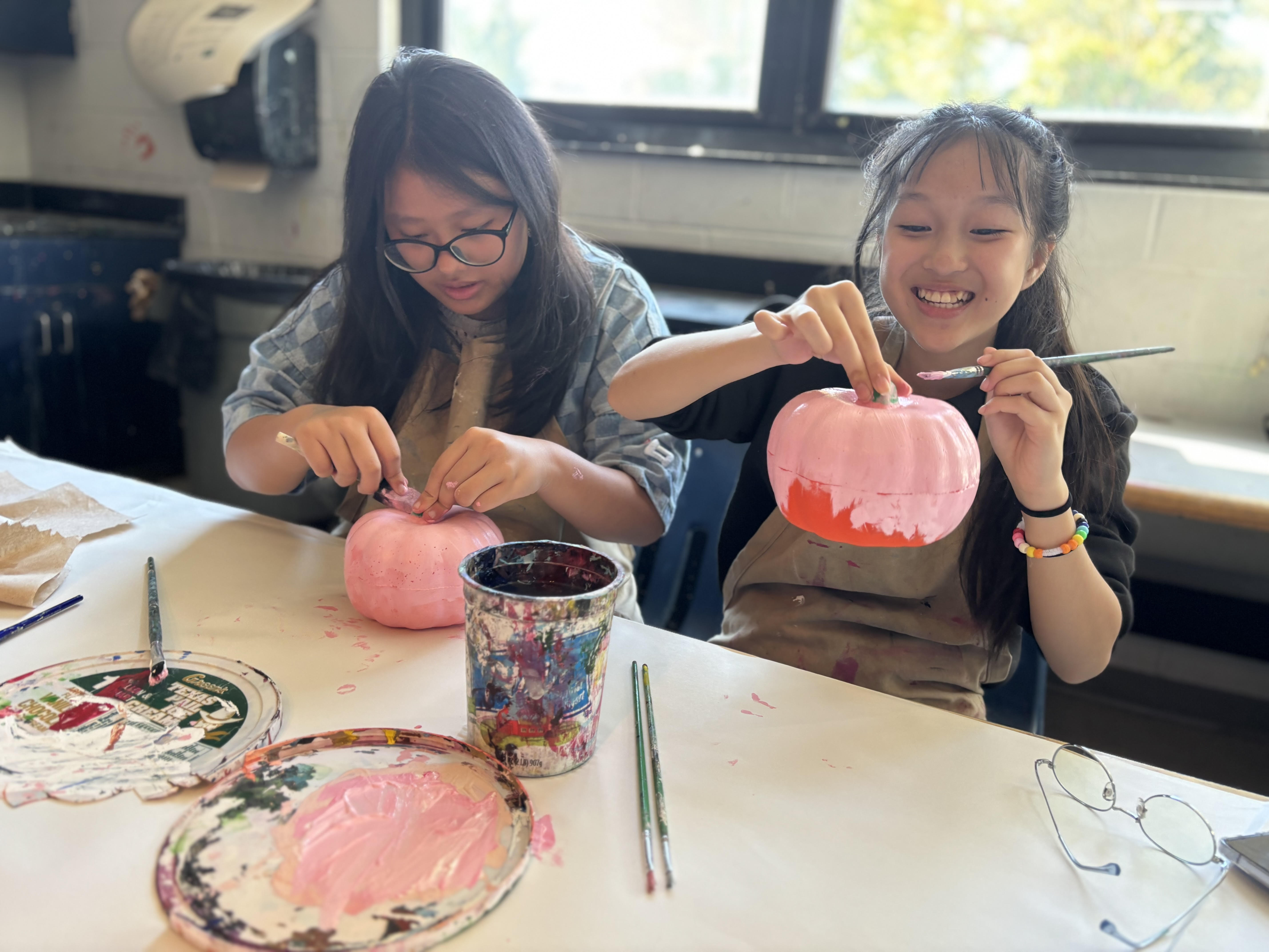 Girls painting pumpkins at a classroom table